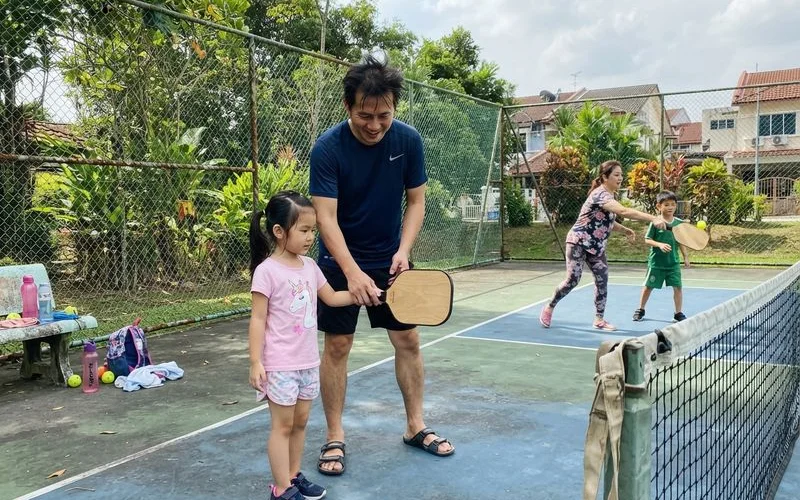 A parent and two children play a casual doubles game together on an indoor pickleball court in Klang Valley