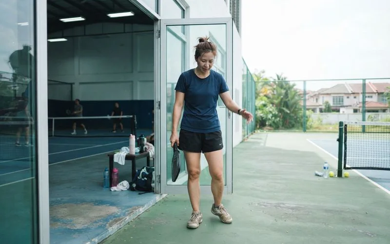 A wide shot comparing an indoor air-conditioned pickleball court on the left and a sunlit outdoor pickleball court on the right, both in Klang Valley