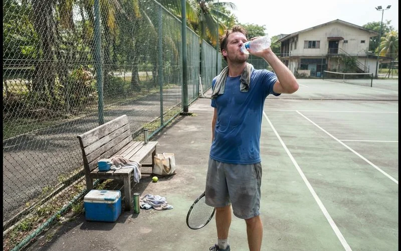 A player pauses to drink water from a bottle beside an outdoor pickleball court in Klang Valley during a bright, sunny afternoon